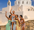Women in mint, blue, yellow, and pink dresses in front of a white church.