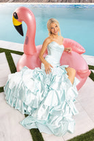 Light blue gown XO085 model poses with flamingo float by pool.