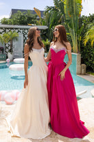 Two women in XO187 Champagne & Fuchsia prom dresses by a pool.